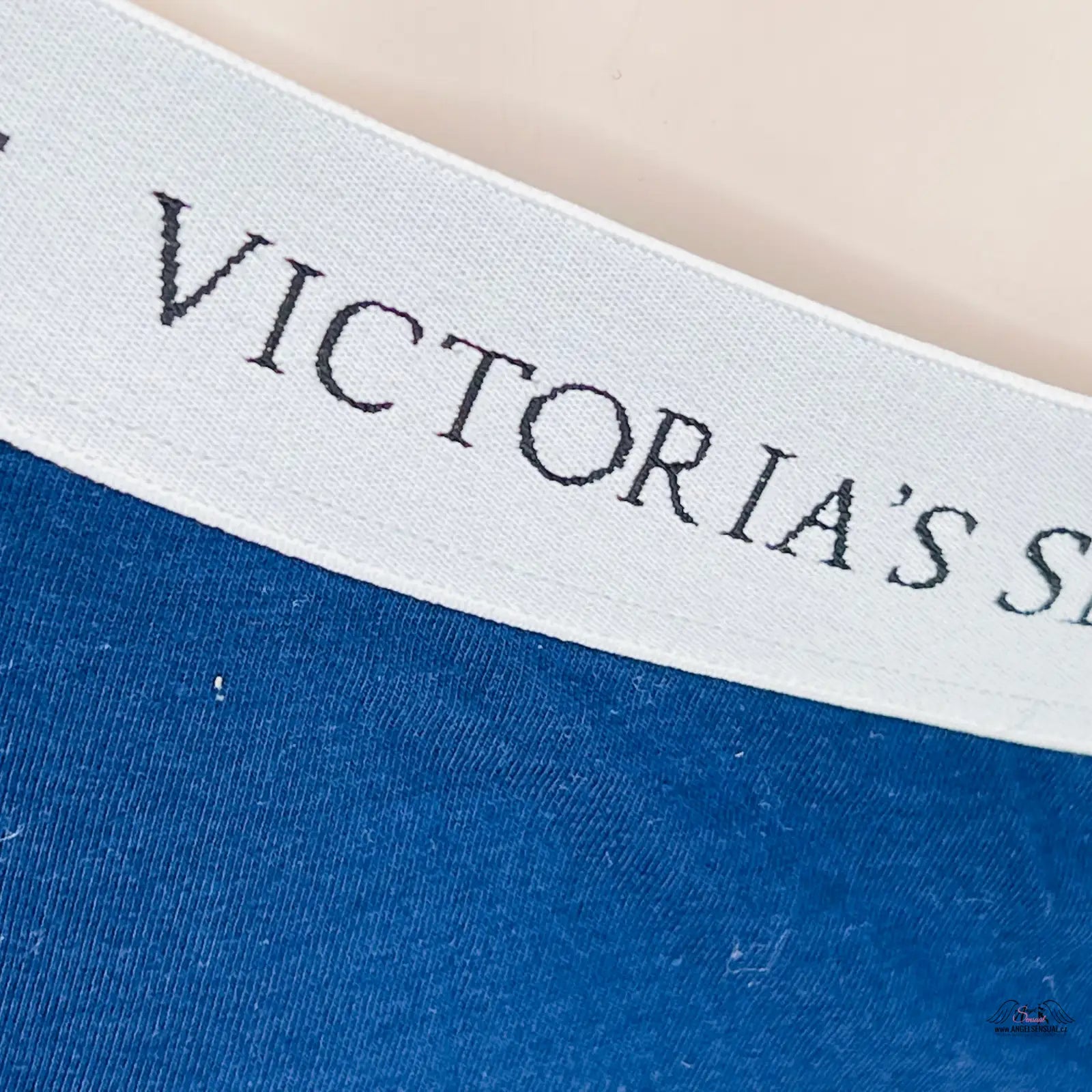 Logo Victoria’s Secret na bílém textilu s modrým pozadím produktu Komfortní Bavlněné Kalhotky pro Celodenní Pohodlí