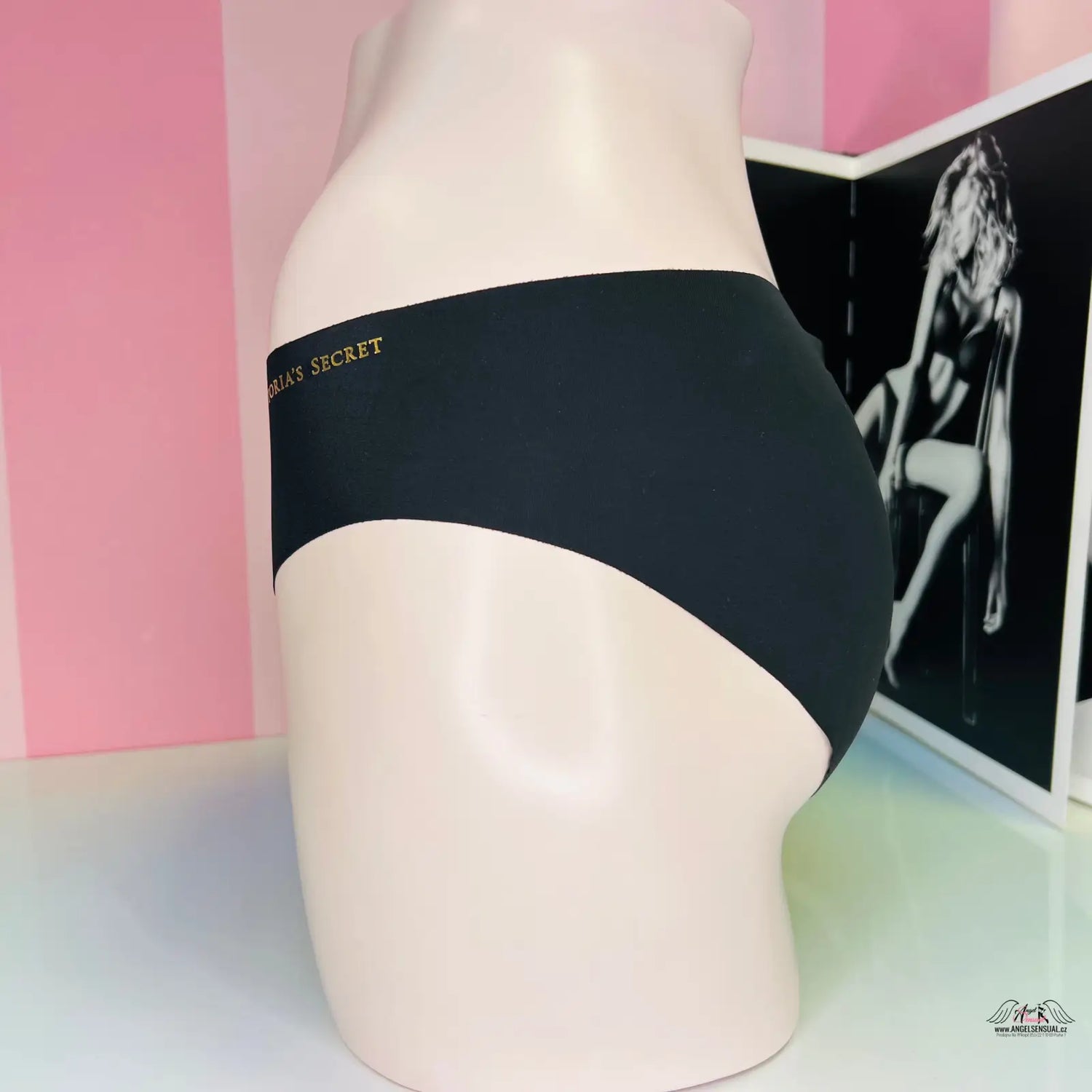 Arafed model in bezešvé kalhotky s zlatým nápisem, černý pás a růžová zeď
