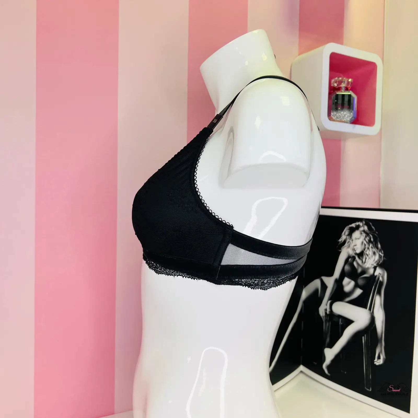 Manekýn s krajkovým červeným bralette s nastavitelnými popruhy na růžové pruhované zdi