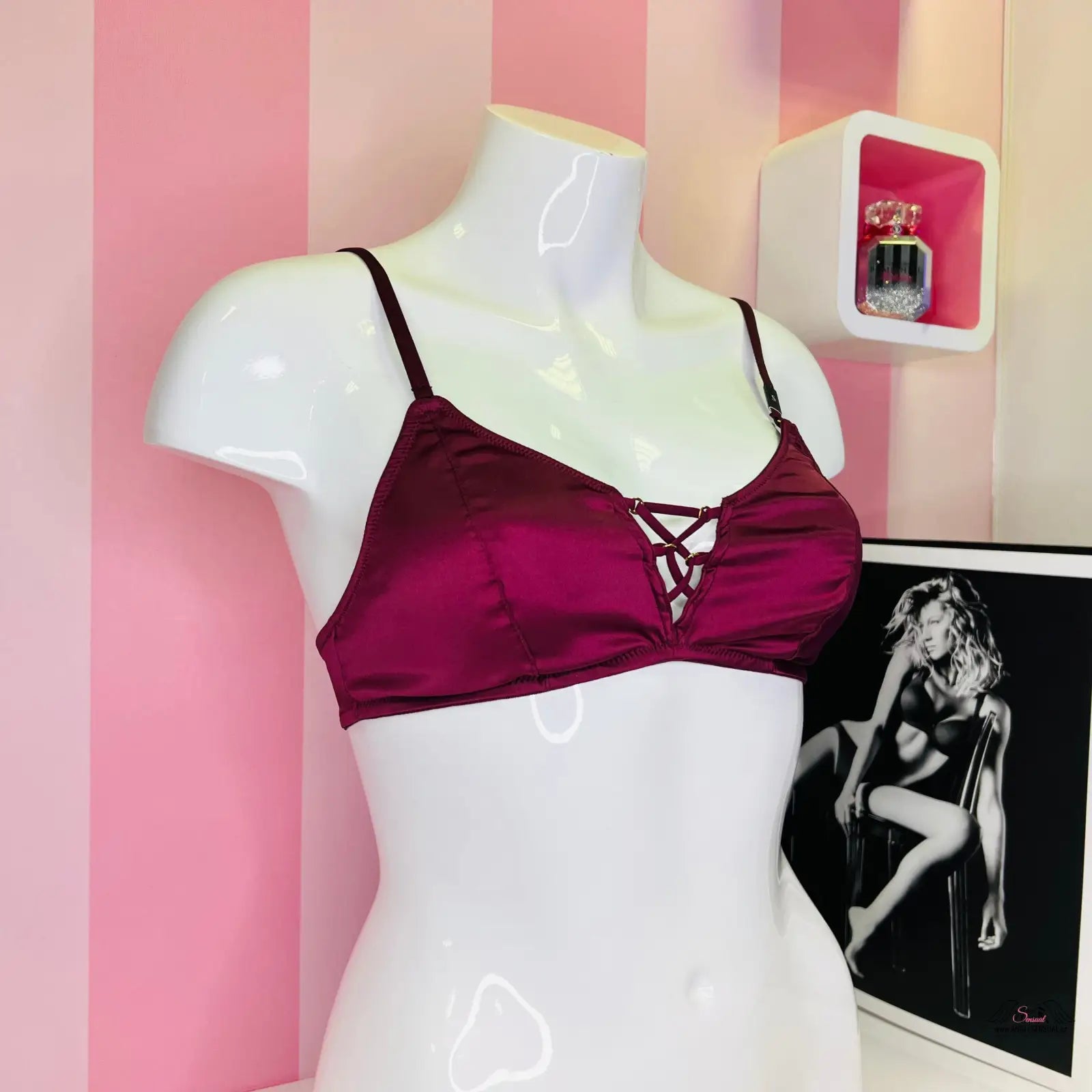 Mannequin v černé lace up bralette s přední aplikací, stojí před růžovou pruhovanou stěnou