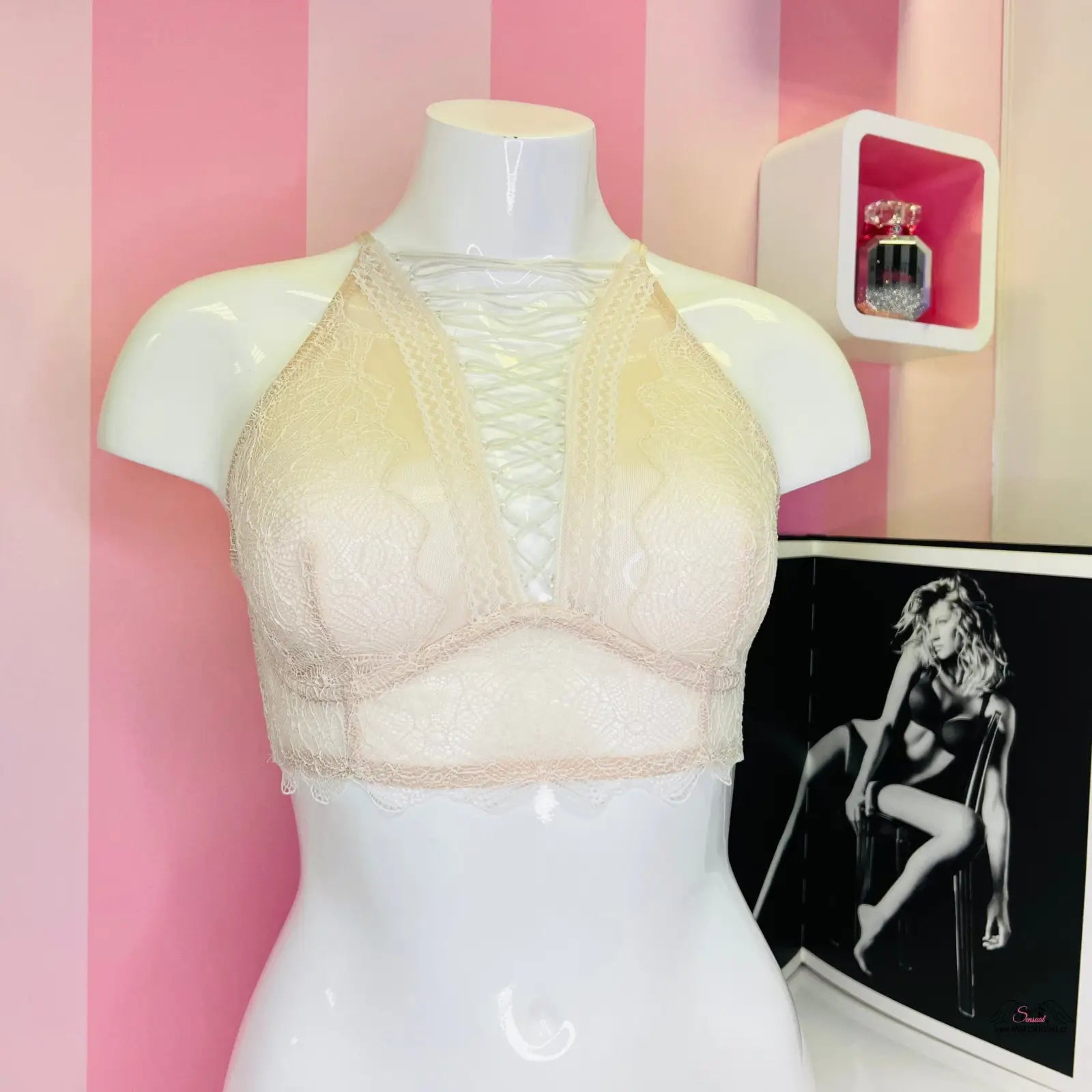 Arafovaný manekýn s bílou podprsenkou Victoria’s Secret s překříženými ramínky na růžové pruhované zdi