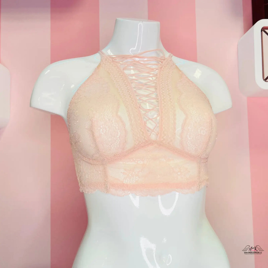 Manekýn s podprsenkou Victoria’s Secret s překříženými ramínky na růžové pruhované stěně