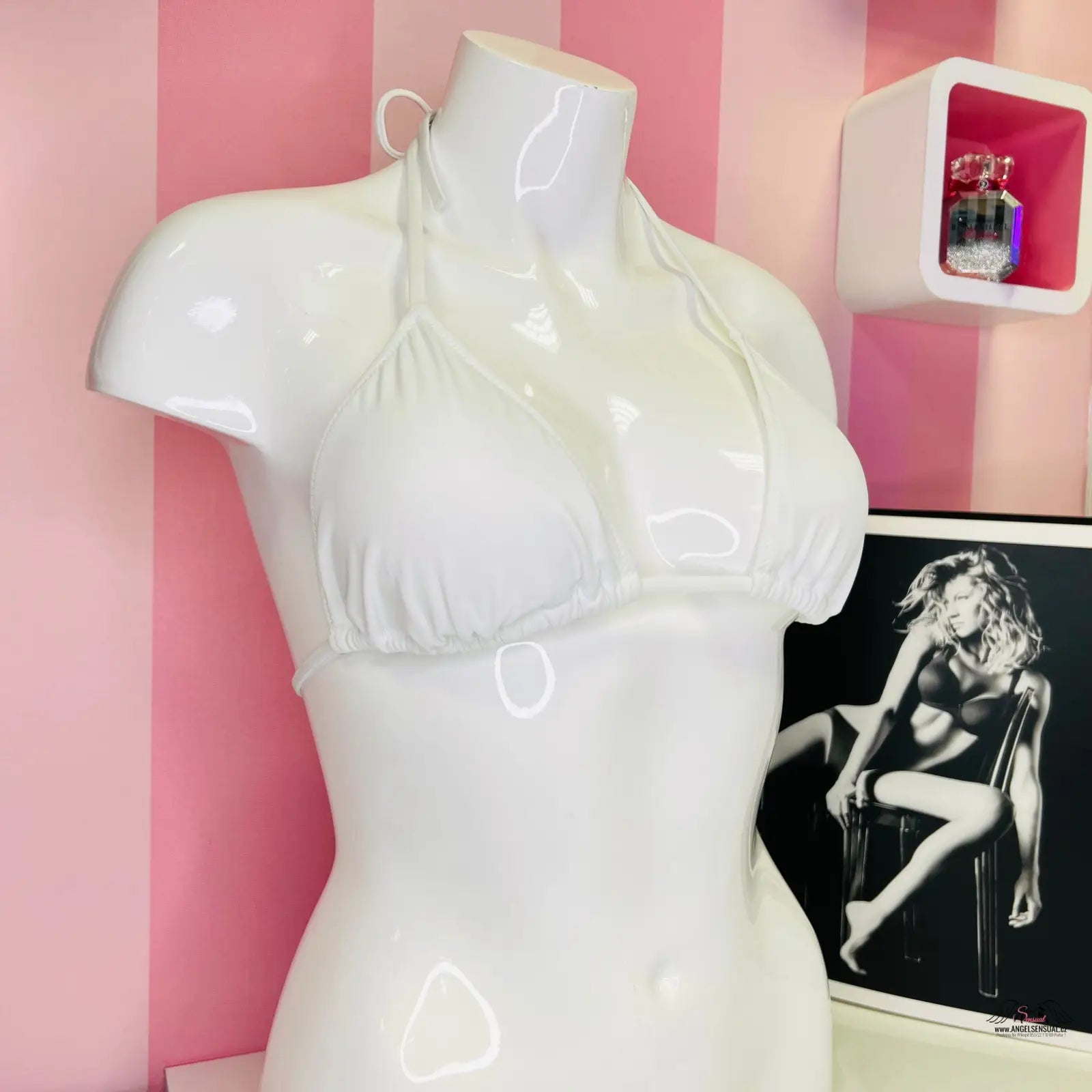 Manekýn s bílým trojúhelníkovým bikiny topem na růžovo-bílé pruhované stěně, stylový plážový vzhled