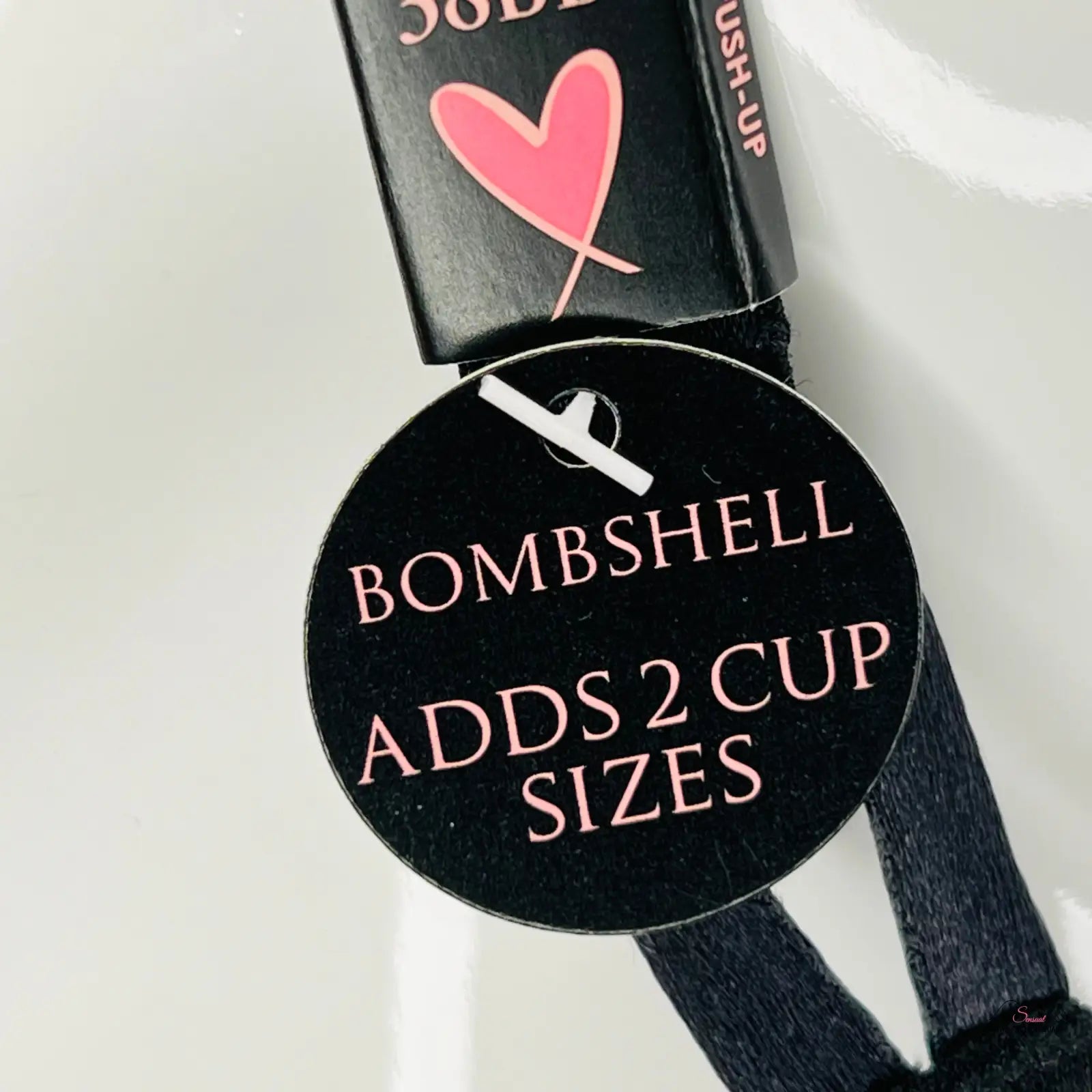 Černá kulatá nálepka s růžovým textem o zvýšení velikosti push up podprsenky Bombshell Push pro sexy dekolt
