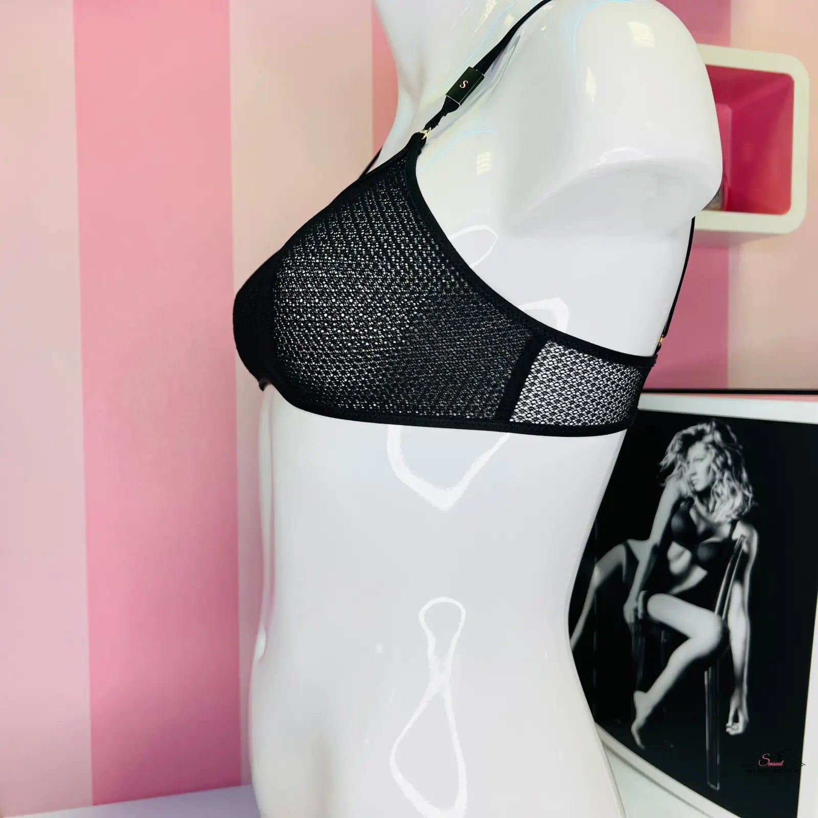 Manekýn s černou svůdnou podprsenkou Victoria’s Secret na růžově pruhované zdi