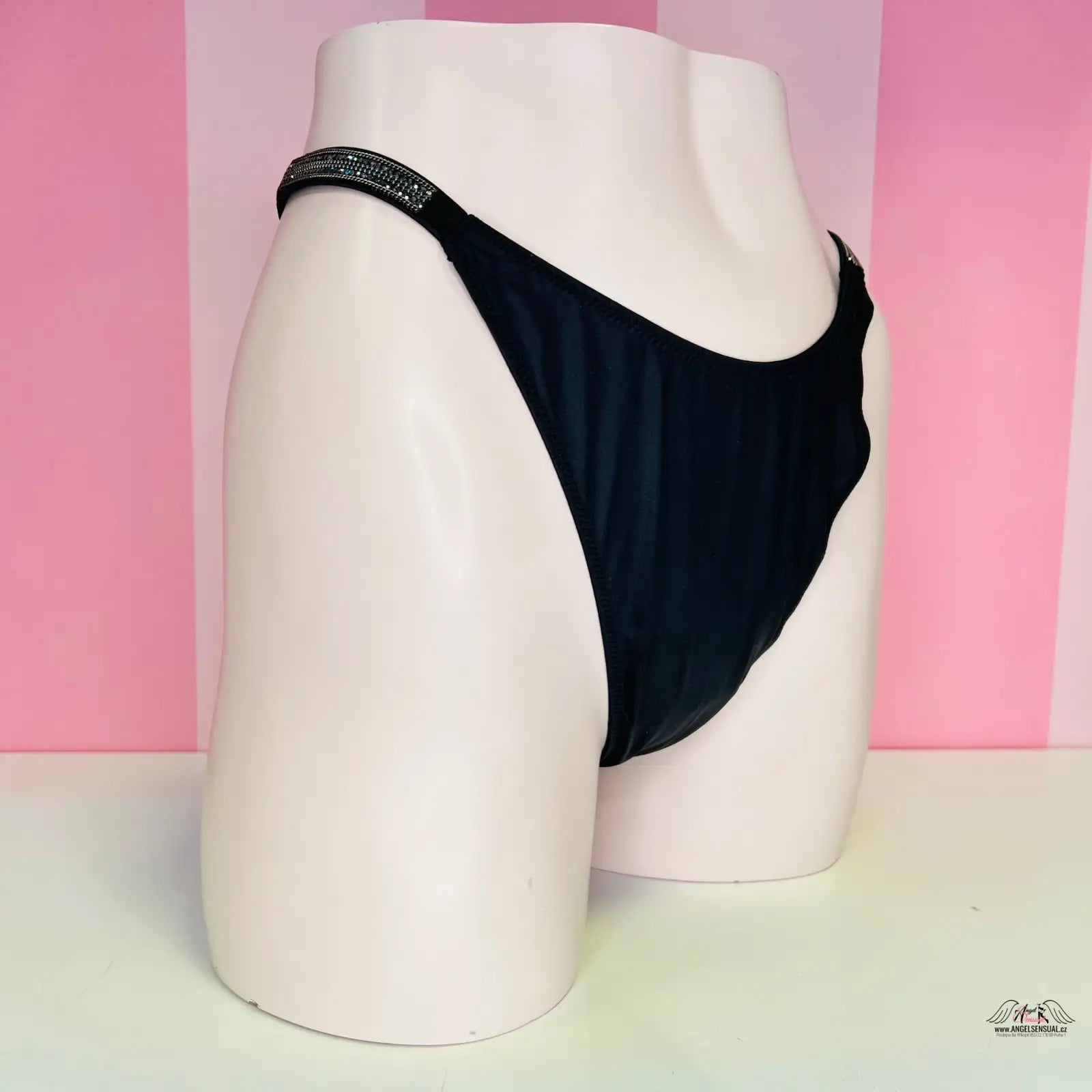 Alt text: Černé tanga s lehce vyšším pasem luxusní na bílém modelu, Victoria’s Secret Tanga s Kamínky