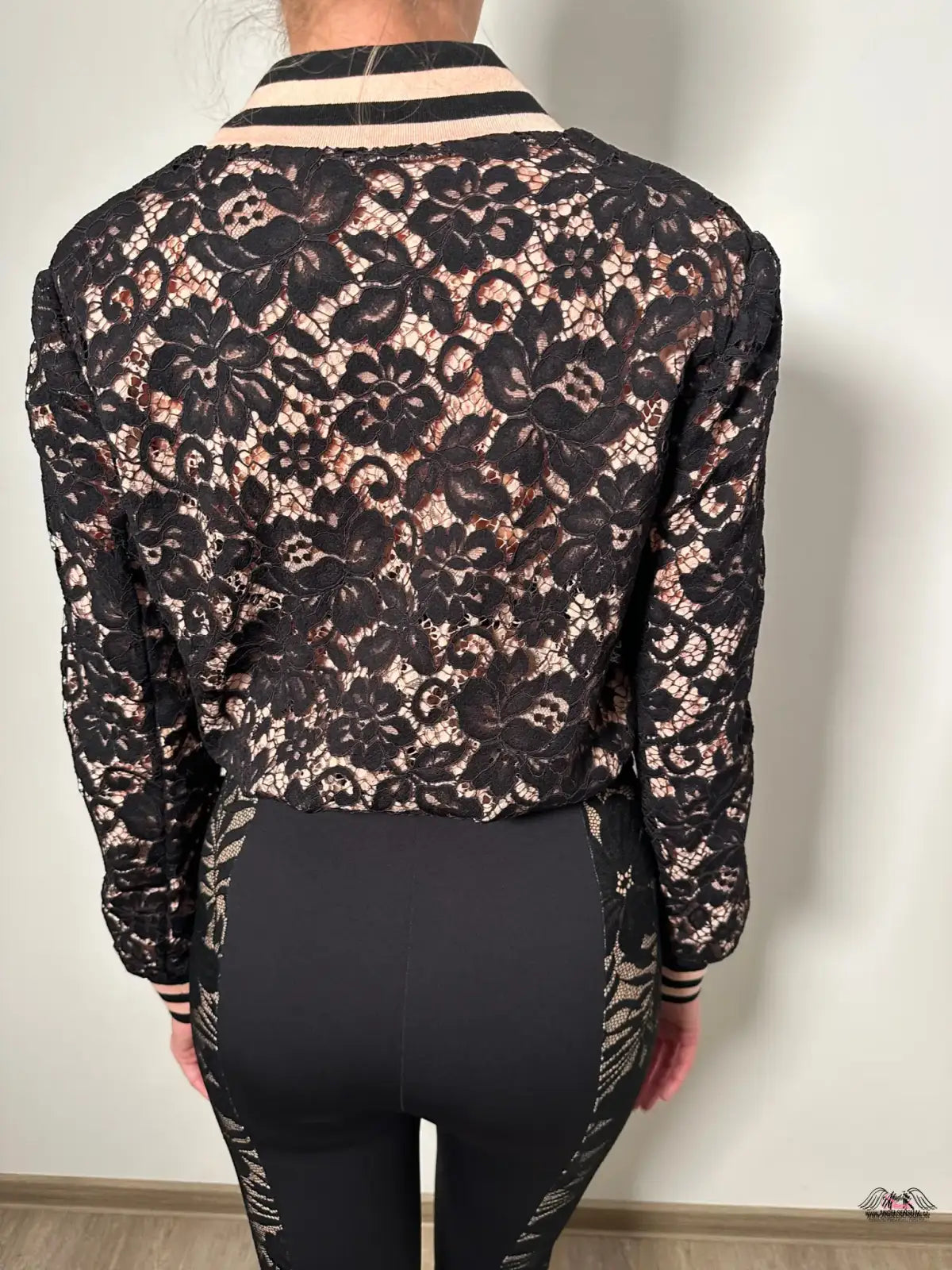 Záda ženy v černém a zlatém květinovém topu s elegantní bundou Codey Bomber