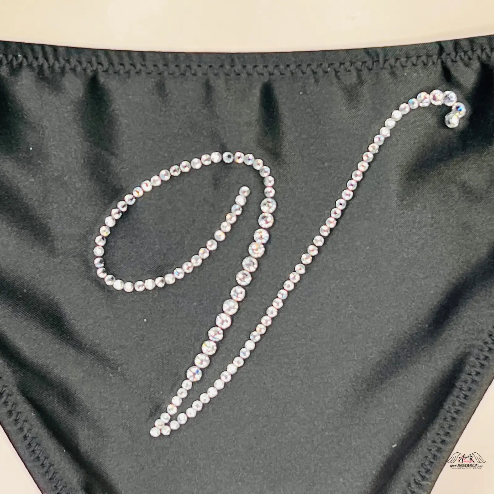 Cursive písmeno V z kamínků na černé textilii Elegantní Hebká Tanga