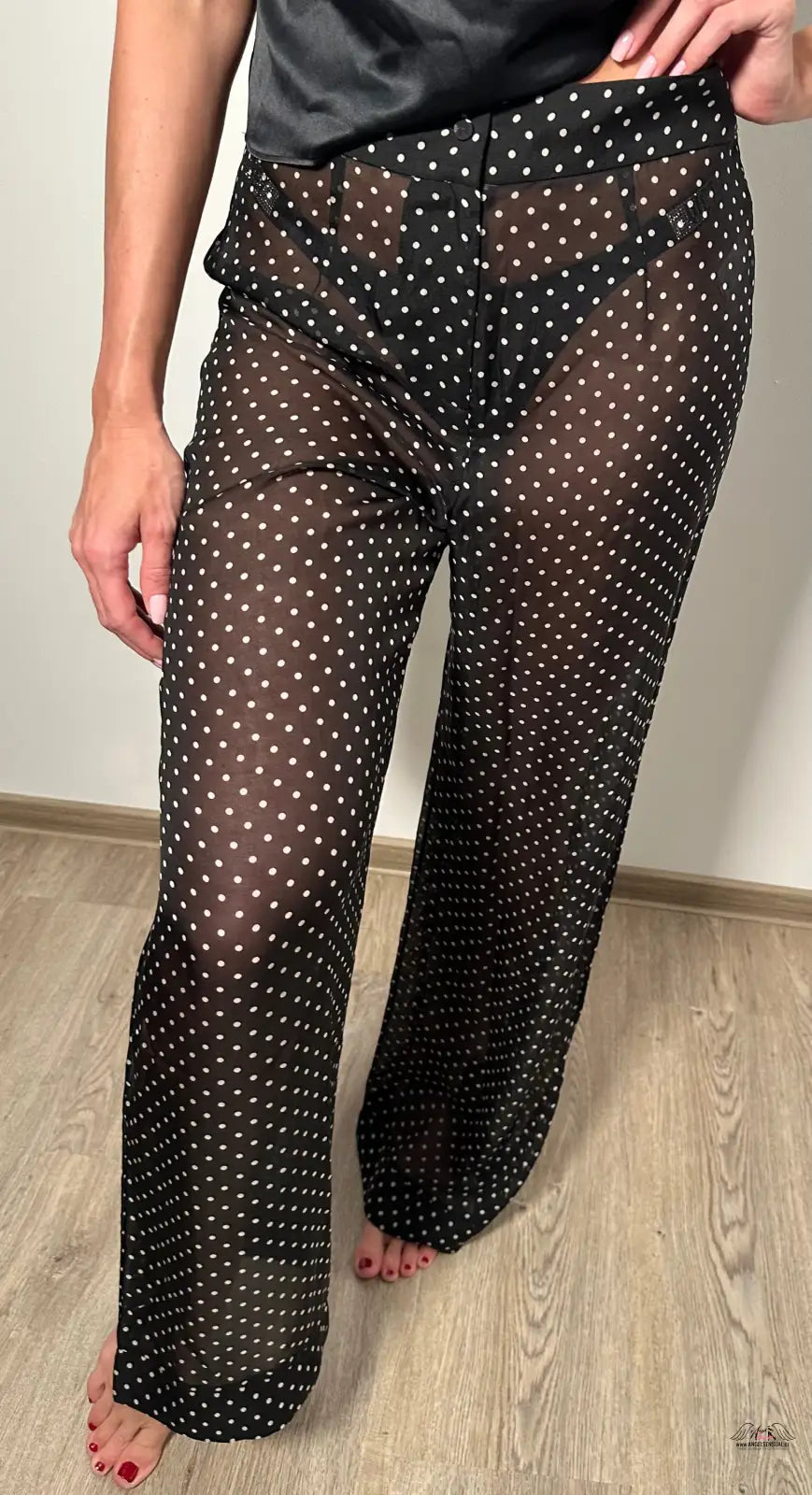 Žena v černých puntíkovaných kalhotách a černém topu prezentuje Stylové Pyžamové Kalhoty Pennie