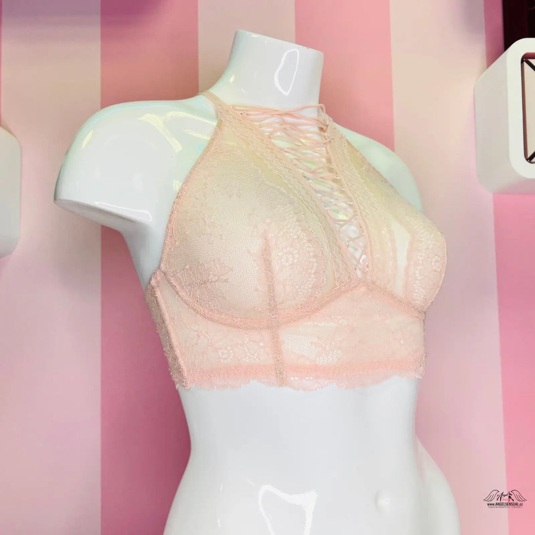 Manekýn s podprsenkou Victoria’s Secret s překříženými ramínky na růžové pruhované stěně