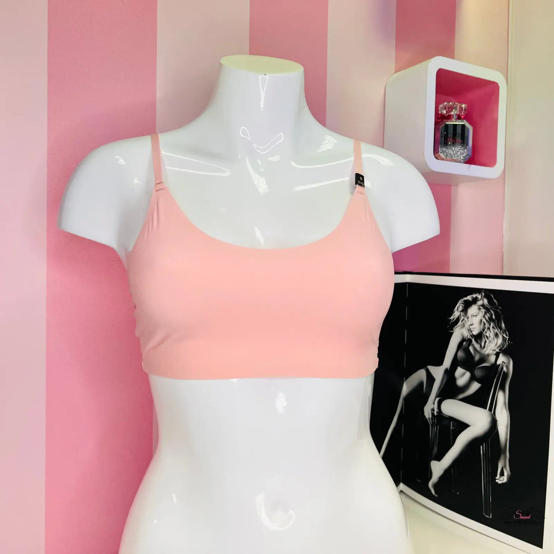 Manekýn s růžovou stylovou braletou Victoria’s Secret na černobílé pruhované tapetě