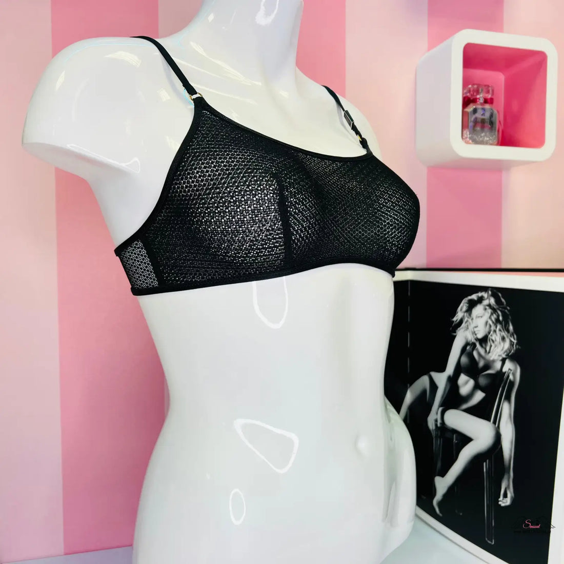 Detail svůdné podprsenky Victoria’s Secret s černým designem na růžové pruhované zdi