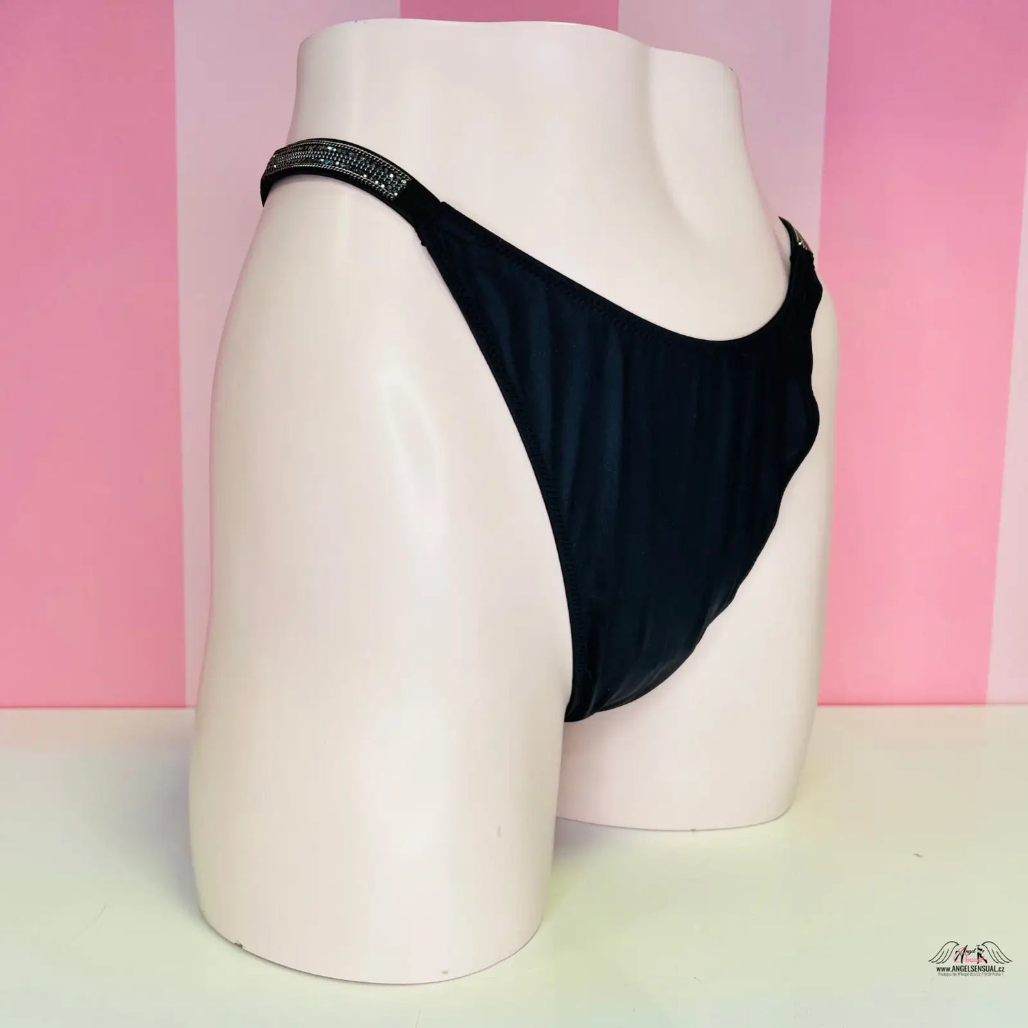 Alt text: Černé tanga s lehce vyšším pasem luxusní na bílém modelu, Victoria’s Secret Tanga s Kamínky