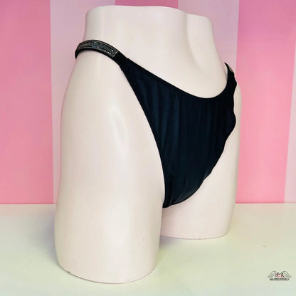 Alt text: Černé tanga s lehce vyšším pasem luxusní na bílém modelu, Victoria’s Secret Tanga s Kamínky